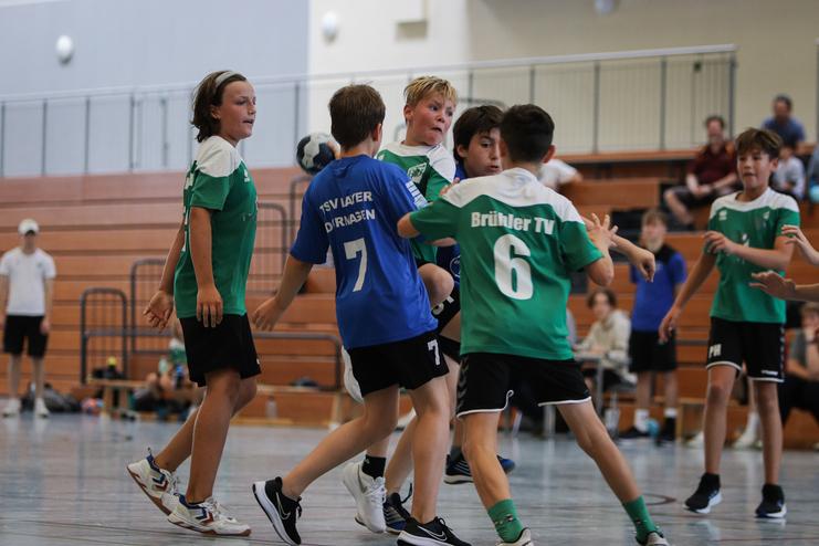 Zwei Handballmannschaften im Wettkampf; Spieler in grün und blau kämpfen um den Ball in einer Sporthalle.