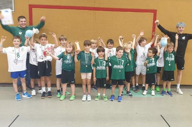 Gruppe von Jugendlichen in Sportkleidung mit Medaillen, die jubeln und feiern in einer Sporthalle.