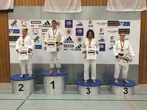 Vier Judoka stehen auf dem Treppchen nach einem Wettkampf, jede mit Medaille und Urkunde in der Hand.