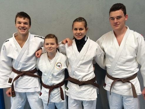 Vier Jugendliche mit braunen Judo-Gürteln posieren in weißen Judo-Anzügen vor einer grauen Wand.