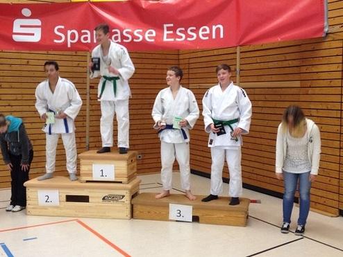 Vier Judoka stehen auf dem Siegertreppchen, während eine Person im Hintergrund sich verneigt.