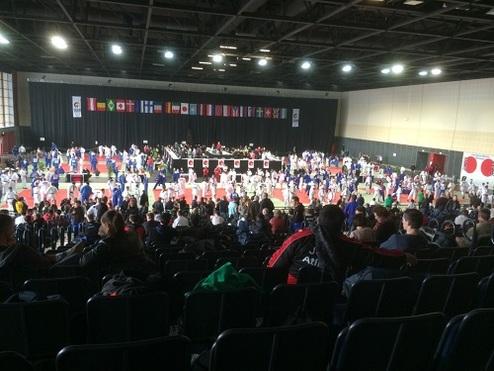 Blick auf eine große Sporthalle mit Karatekämpfern in weißen und blauen Anzügen während eines Wettkampfs.