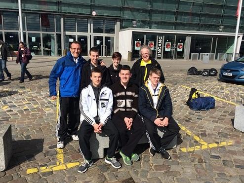 Gruppe von sieben Personen in Sportkleidung sitzt auf einem Steinblock vor einem modernen Gebäude.