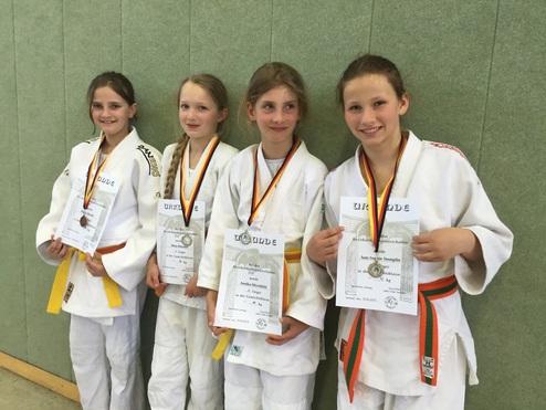 Vier junge Judokas in weißen Judokimonos halten Medaillen und Urkunden nach einem Wettkampf.