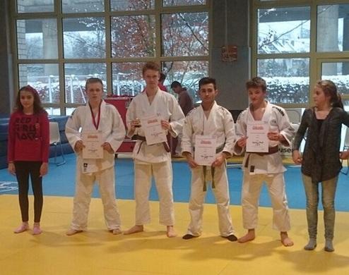 Fünf Jugendliche in Judokleidung halten Urkunden in einer Sporthalle mit gelbem Mattenboden.