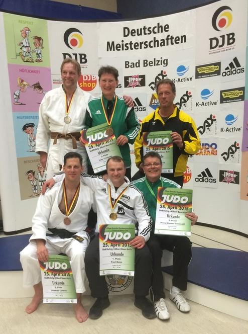 Sechs Judokas mit Medaillen und Urkunden posieren in Siegerpose vor einem Banner der Deutschen Meisterschaften.