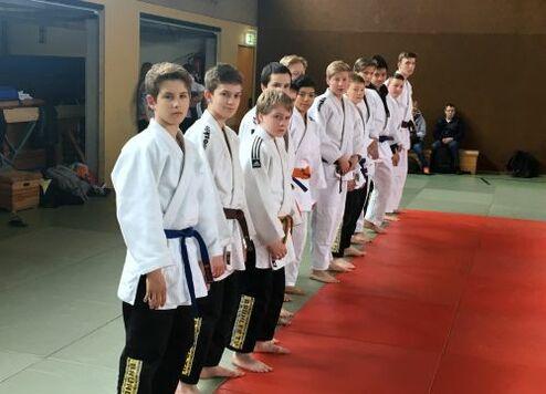 Gruppierung von Judoka in weißen Anzügen, die in einer Reihe auf einer Tatami stehen, bereit zum Training.