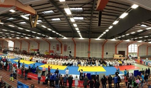 Panoramablick auf eine Sporthalle mit Judowettkämpfen, Teilnehmer in weißen Ganzkörperanzügen auf blauen Matten.