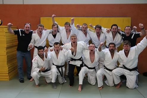 Gruppe von Judokas in weißen Gi-Kostümen jubelt zusammen auf einer Judomatte.