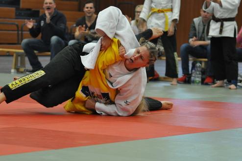 Zwei Athletinnen kämpfen auf einer Judomatte, eine im weißen und die andere im gelben Judoanzug.
