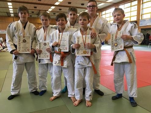Sechs Kinder in Judoanzügen halten stolz ihre Urkunden und Medaillen in einem Sportzentrum.