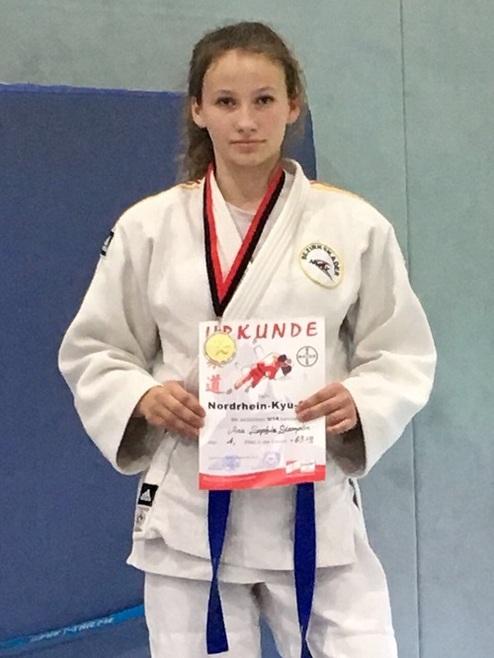 Mädchen in Judo-Gi hält Urkunde für den Nordrhein-Kyū im Sportbereich mit blauer Band und Medaille.