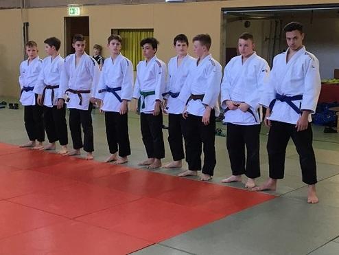 Junge Judoka in weißen und blauen Gi stehen auf einer Matte in einer Kampfsporthalle bereit.