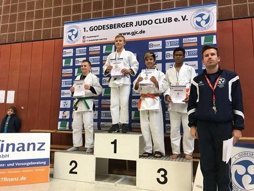 Junge Judoka stehen auf dem Siegertreppchen und halten Medaillen sowie Urkunden in der Hand.