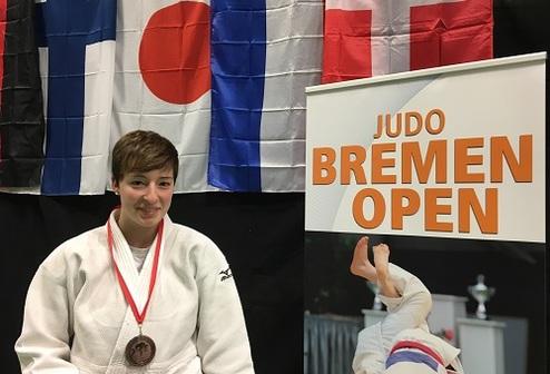 Junge Judoka mit Medaille sitzt vor Flaggen und Banner des Judo Bremen Open.