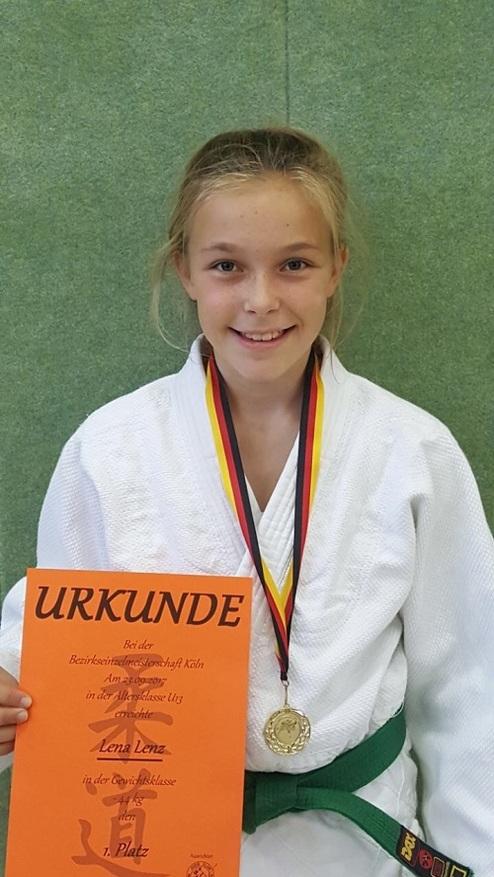 Mädchen in Judogi mit Medaille und Urkunde für den ersten Platz bei einem Judowettkampf, Hintergrund in grün.