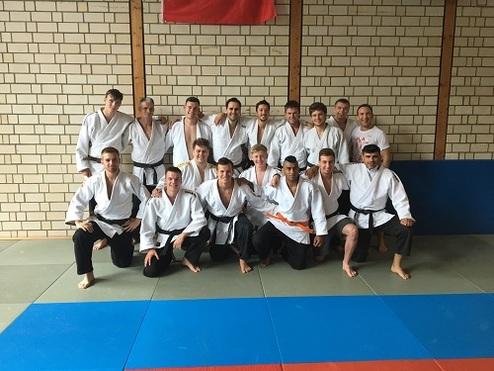 Gruppenfoto von 14 Personen in Judoanzügen, auf einer matten Fläche in einer Turnhalle.