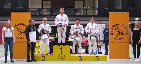 Junge Judoka stehen auf dem Siegerpodest, umgeben von Banner des DSC Wanne-Eickel und jubelnden Zuschauern.