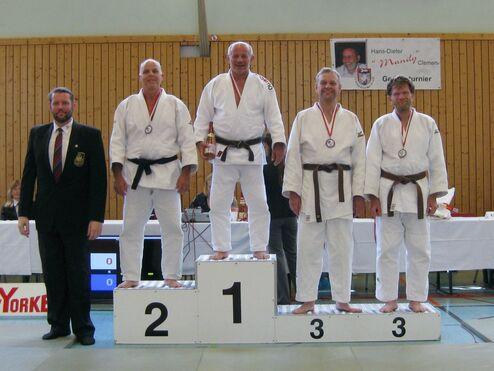 Fünf Judo-Kämpfer auf einem Siegertreppchen, Medaillen umgehängt, bei einer Wettkampfveranstaltung in einer Halle.