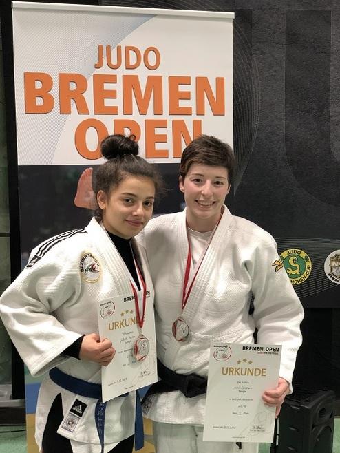Zwei Judokas in Uniform halten ihre Medaillen und Urkunden vor einem Banner der Bremener Judo Open.