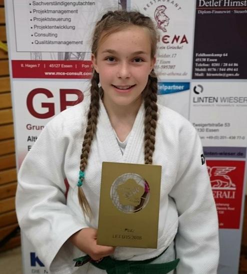 Mädchen im Judoanzug hält eine goldene Medaille für den ersten Platz in einem Wettkampf.
