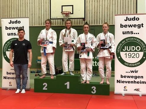 Siegerinnen stehen auf dem Podium, umgeben von Judo-Werbebannern, bei einem Wettkampf in Nievenheim.