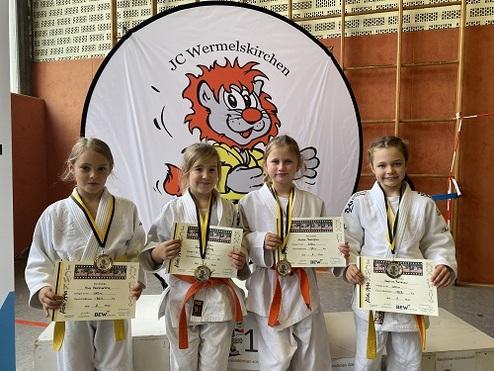 Vier junge Judoka in weißen Anzügen halten Siegerurkunden und Medaillen vor einem Banner des JC Wermelskirchen.
