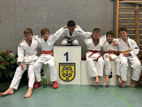 Sechs Jungs in Judogis posieren um eine Siegertreppe mit der Nummer 1 im Hintergrund.