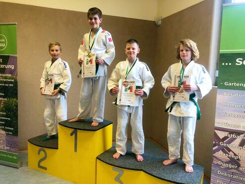 Vier Kinder in Judogi stehen auf dem Siegerpodest mit Urkunden und Medaillen in der Hand.