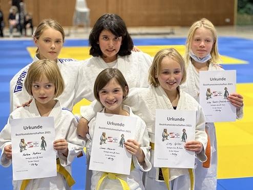 Sechs Kinder in Judoanzügen halten Gewinnerurkunden auf einer Judomatte. Hintergrund in Gelb und Blau.
