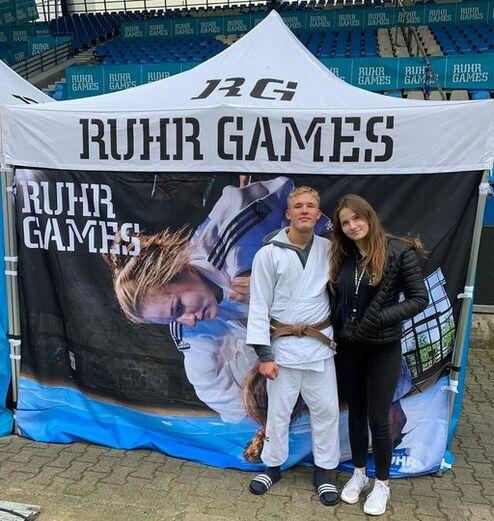 Junge im Judogi mit braunem Gürtel und Mädchen in schwarzer Jacke stehen vor einem Zelt mit „Ruhr Games“-Banner.