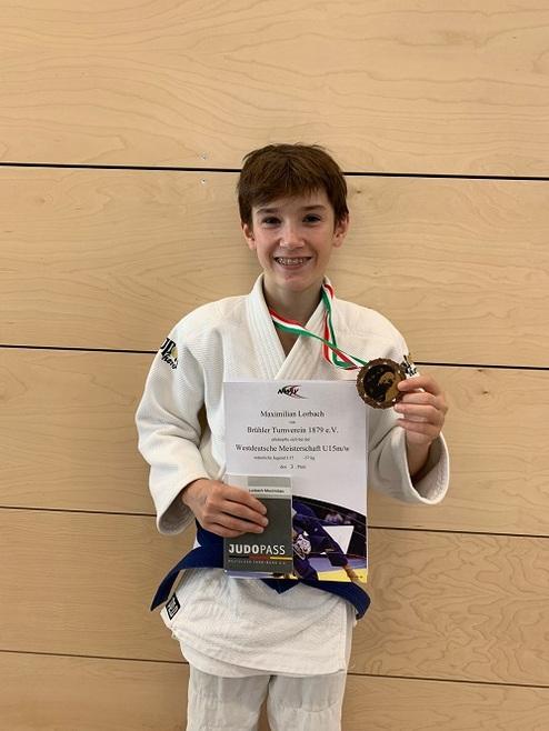 Junge in Judokleidung hält Medaille und Urkunde vor holzvertäfeltem Hintergrund.