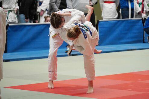Zwei Judokas in weißen Anzügen kämpfen auf einer Tatami, während einer die Technik eines Wurfs anwendet.