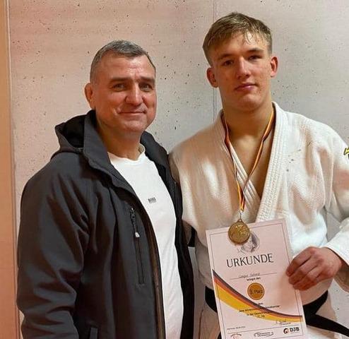 Zwei Männer in Sportbekleidung, einer mit Medaille und Urkunde für den 3. Platz im Judo.