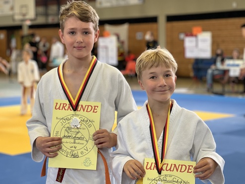 Zwei Jungen in Judogi halten Urkunden für den ersten Platz bei den Bezirksmeisterschaften in Köln.