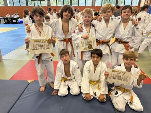 Gruppe von acht Jungen in Judokas, die Medaillen und Urkunden beim Koga Cup präsentieren. Judomatte im Hintergrund.