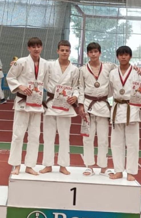 Vier Jugendliche in Judoanzügen stehen auf dem Siegerpodest und halten Zertifikate und Medaillen.