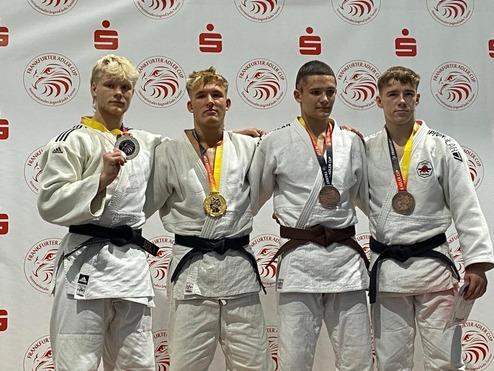 Vier Judoka in Uniform stehen mit Medaillen auf einem Wettbewerbspodium vor einem Banner des Frankfurter Adler Cups.
