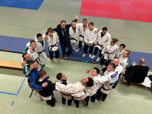 Gruppennahaufnahme von Judokas in weißen Judogis, lächelnd auf einer Trainingsmatte versammelt.