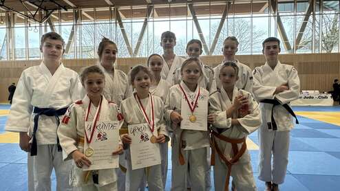 Gruppe junger Judoka in weißen Anzügen, einige halten Medaillen und Urkunden, auf einer blauen Judomatte.