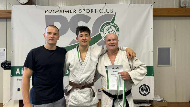Drei Männer stehen vor einem Banner des Pulheimer Sport-Clubs, einer hält eine Urkunde in der Hand.