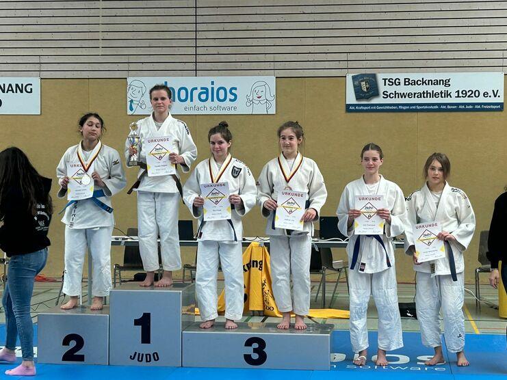 Sechs Judoka auf dem Siegertreppchen mit Urkunden und einem Pokal in einer Sporthalle.