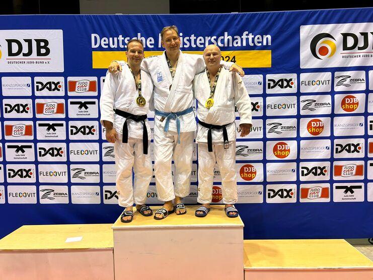 Drei Judoka mit Medaillen stehen auf dem Siegerpodest vor einem Sponsorenbanner bei den Deutschen Meisterschaften 2024.