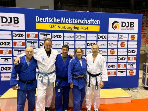 Fünf Judokas in blauen und weißen Judoanzügen stehen vor einem Werbebanner der Deutschen Meisterschaften U30.