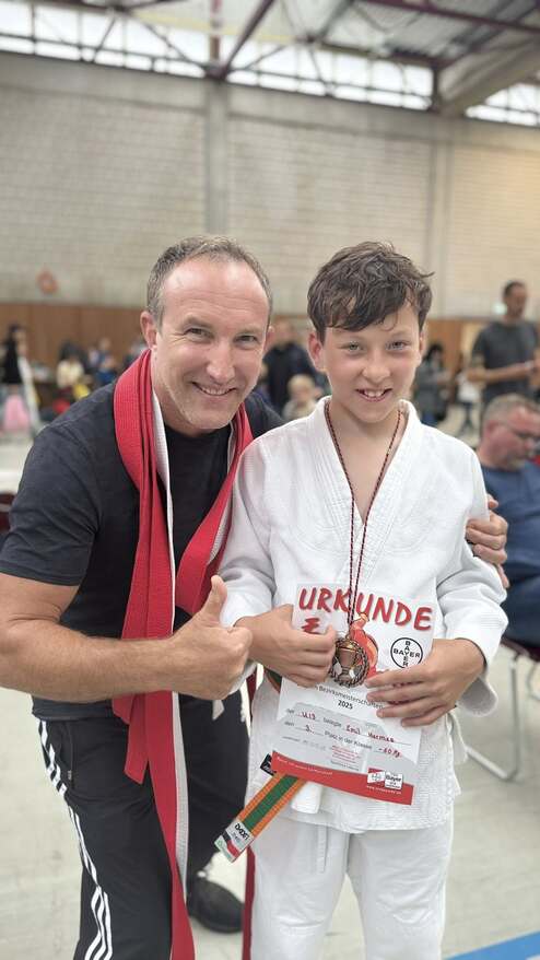 Lächelnde Personen im Judoanzug und mit Urkunde, eine Beförderung bei einem Wettkampf.