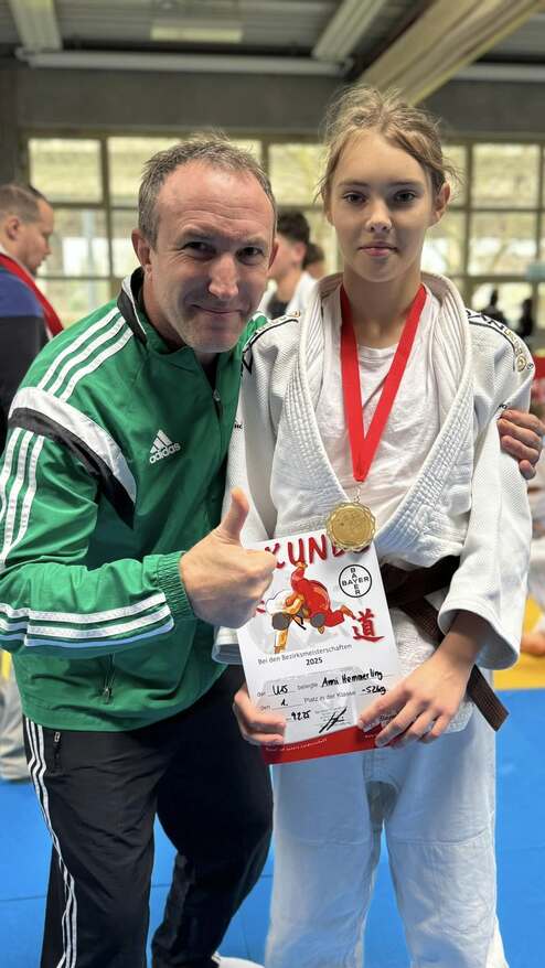 Trainer posiert mit erfolgreicher Judokämpferin, die eine Urkunde und Goldmedaille nach einem Turnier hält.