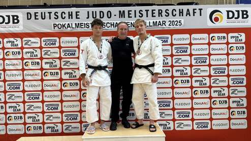 Drei Judoka mit Medaillen posieren für ein Foto auf dem Siegerpodest vor einer Sponsorenwand.