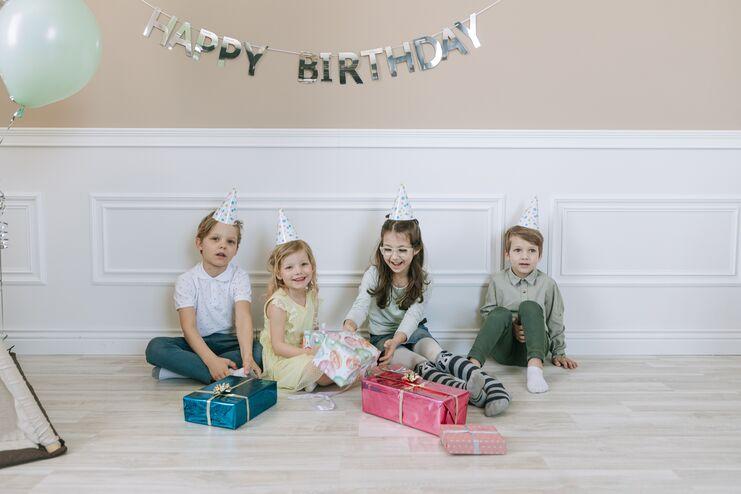 Geschenketausch Four kids in party hats celebrating a birthday with gifts and smiles.