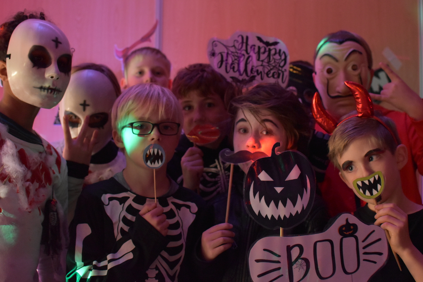 Gruppe von Kindern in Halloweenkostümen mit Masken und Requisiten, darunter ein Schild mit der Aufschrift „Boo“.