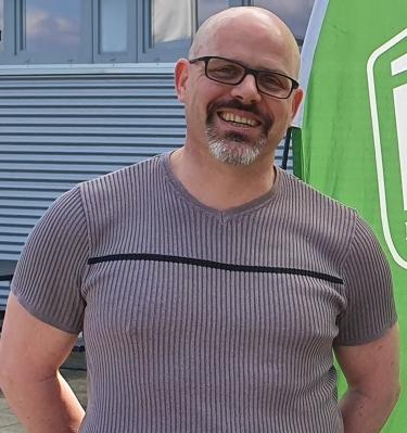 Zwei Personen stehen lächelnd vor einem Eingang, neben einem grünen Banner des Brühler Turnvereins.